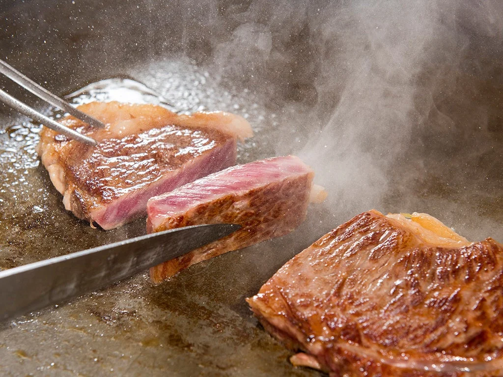 熱い鉄板の上でジューシーなステーキが焼かれている様子