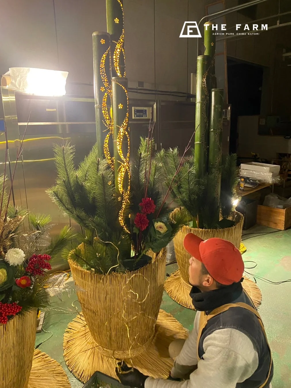 THE FARMにて、従業員が竹筒に施された美しい光の装飾と、松の葉や花を組み合わせた大きな飾り付けを準備している様子です。冬のイベントに向けた準備と思われます。