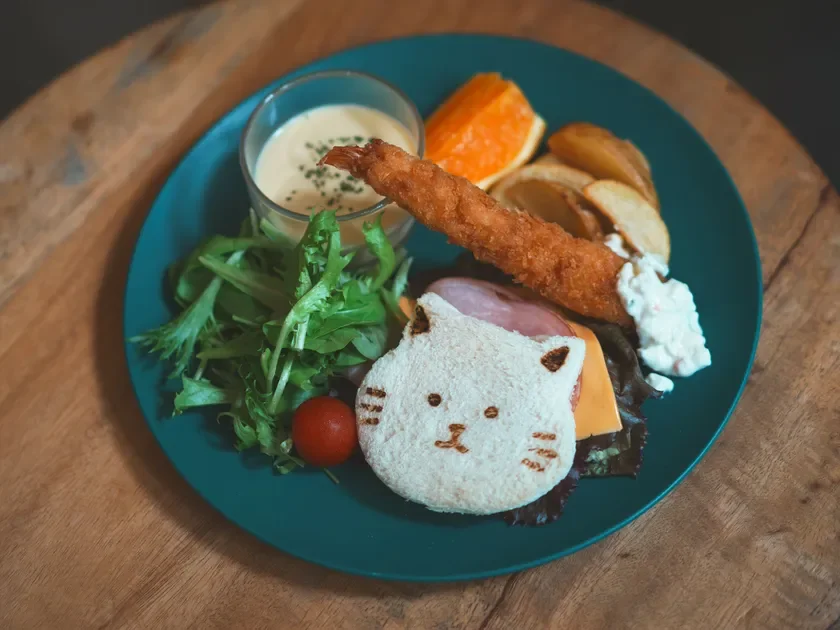 猫の形をした可愛いサンドイッチをメインに、エビフライ、サラダ、ポテト、オレンジなどが盛り合わせられた、彩り豊かなプレートランチです。カフェのような雰囲気で食欲をそそります。