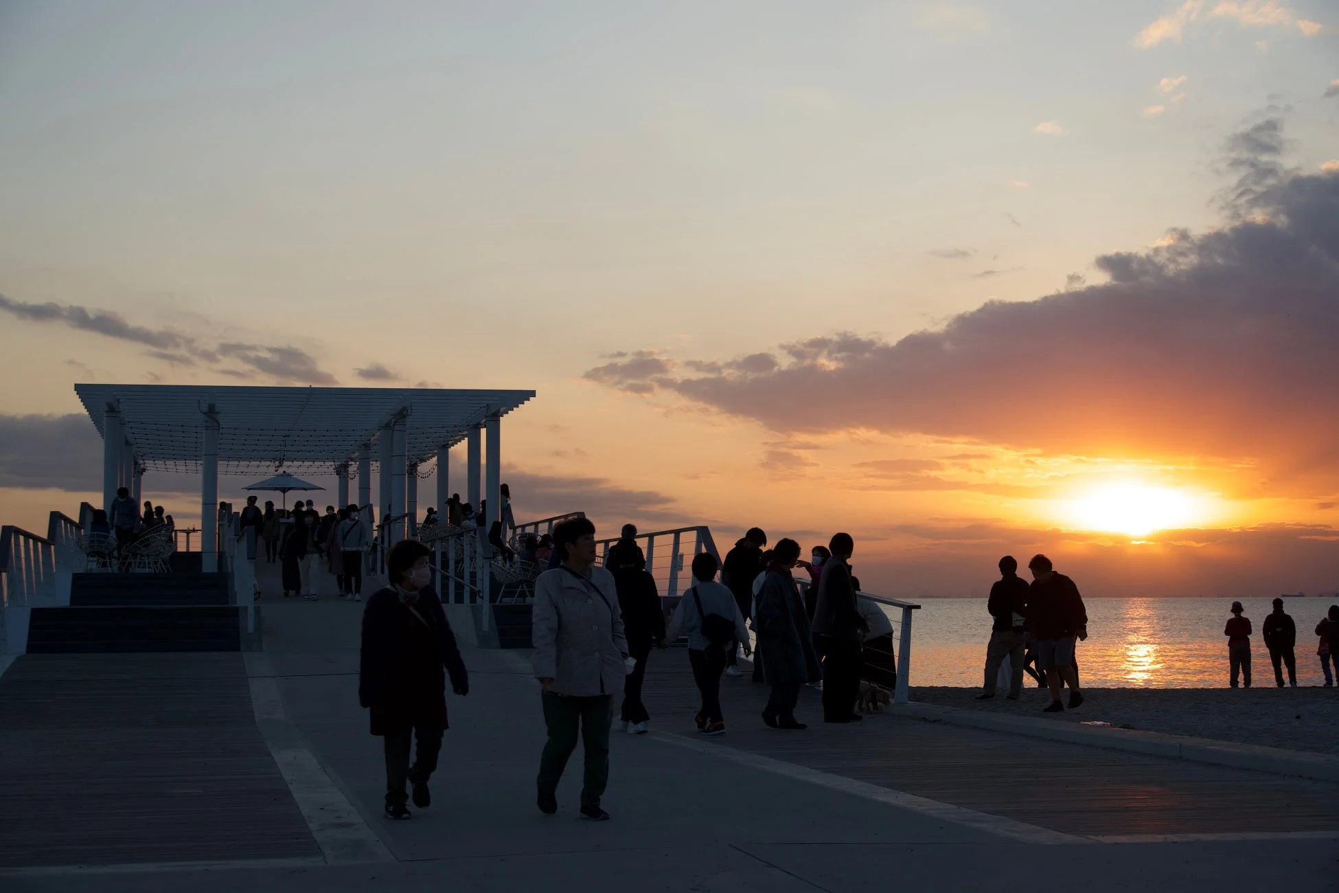 夕焼けのビーチで、多くの人々が桟橋や砂浜を散策