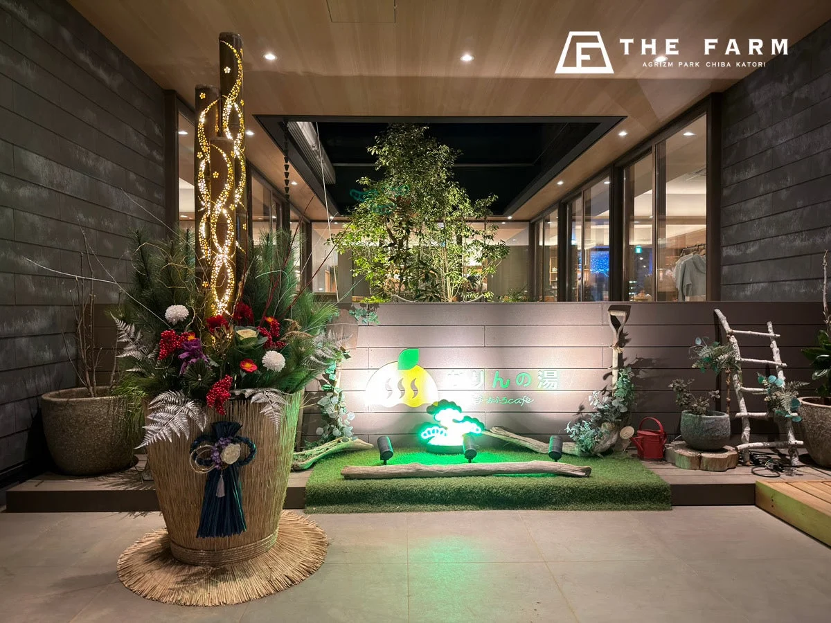 THE FARMのエントランスを夜間に撮影した画像。豪華な和風の装飾と「かりんの湯」「ふかふかcafe」のネオンサインが特徴的で、モダンな建物が温かく魅力的な雰囲気を演出しています。