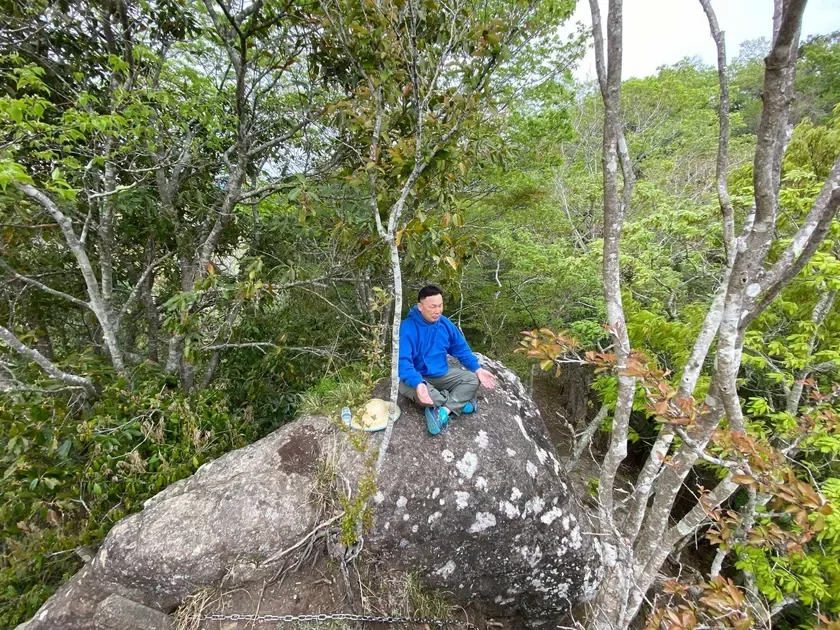 森の中の大きな岩に座る男性