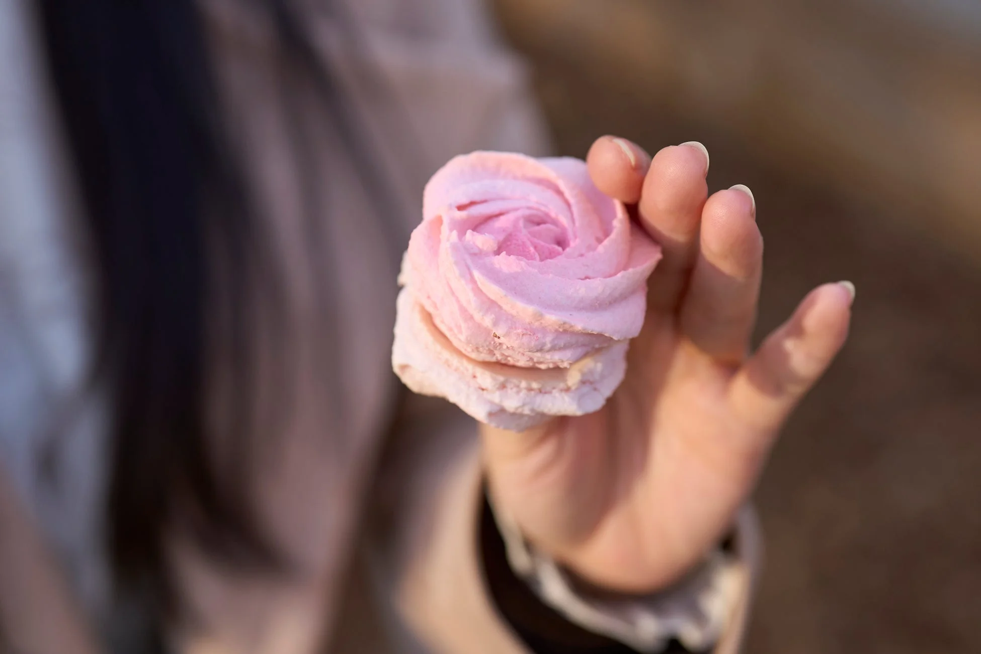 手のひらに乗せられた、渦巻き状の可愛らしいピンク色のデザートのクローズアップです。柔らかそうな質感と、背景のぼかしが優しい雰囲気を醸し出しています。