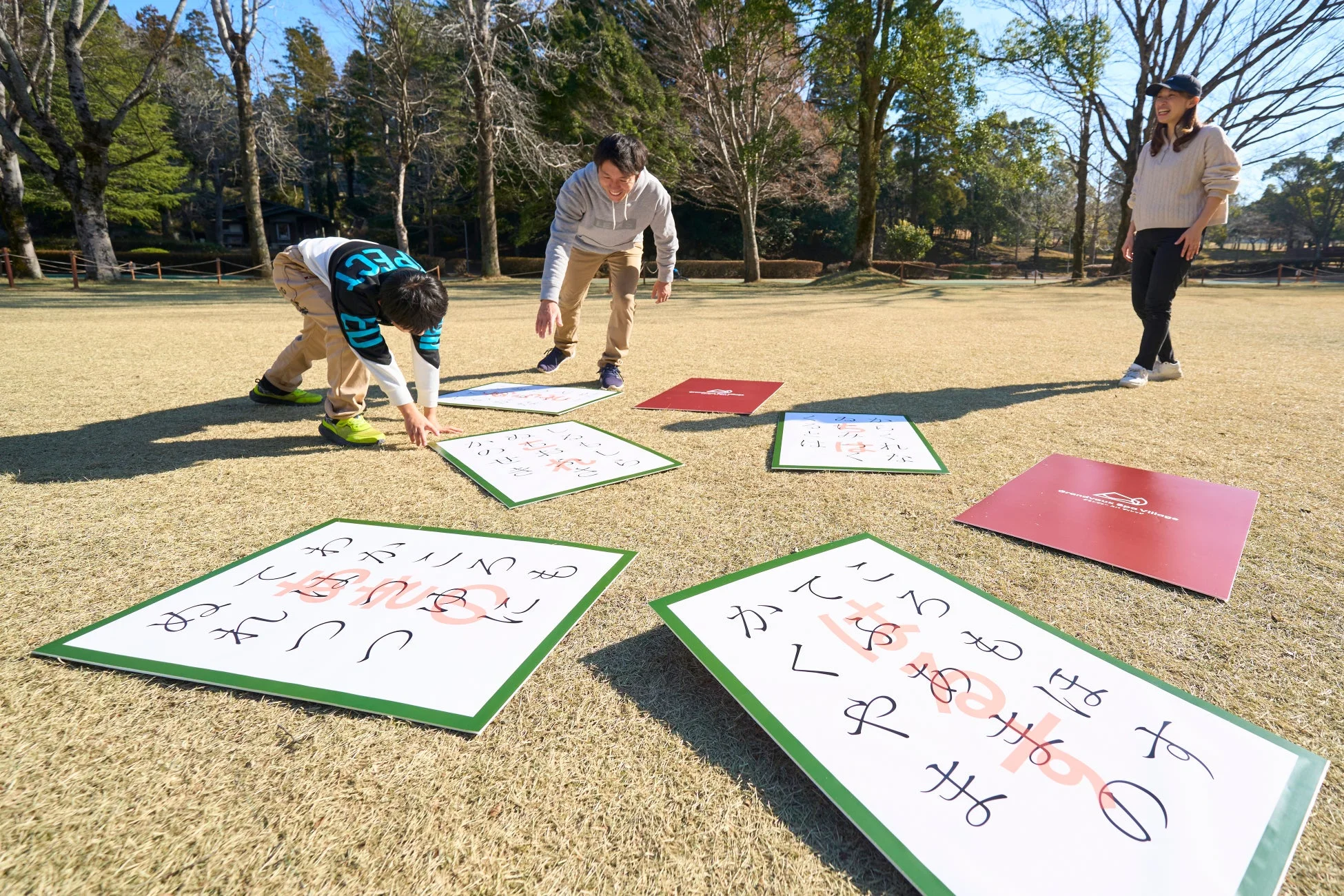芝生の上でジャンボかるたを楽しむ家族