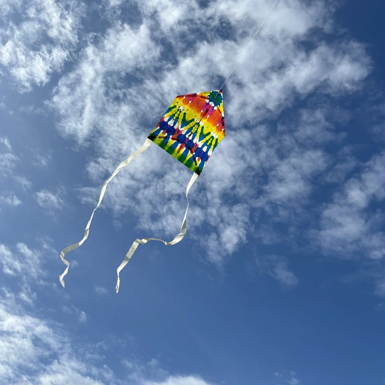 青空に舞い上がるカラフルなタイダイ柄の凧