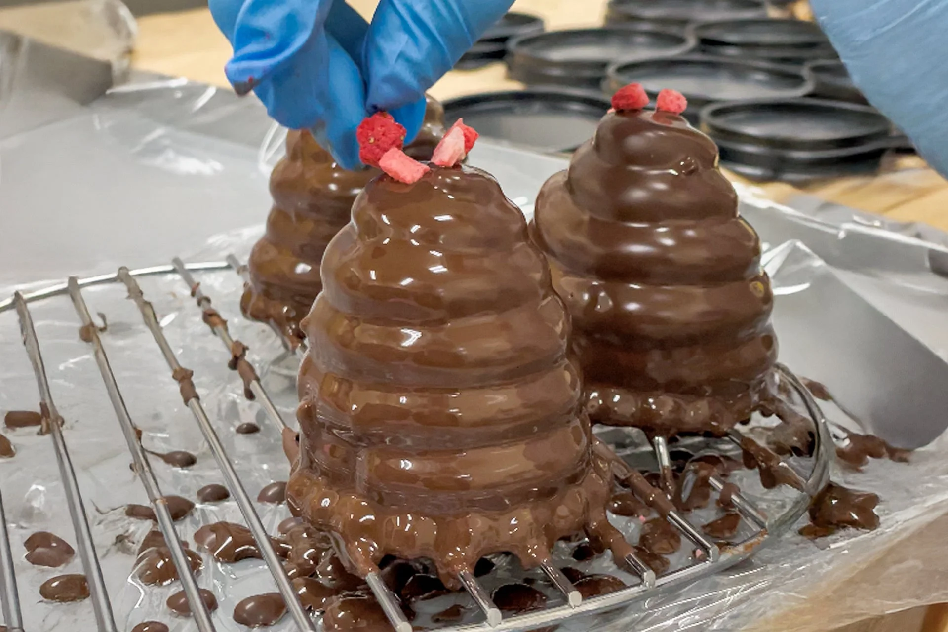 チョコレートでコーティングされたデザートにフリーズドライのイチゴをトッピングする様子