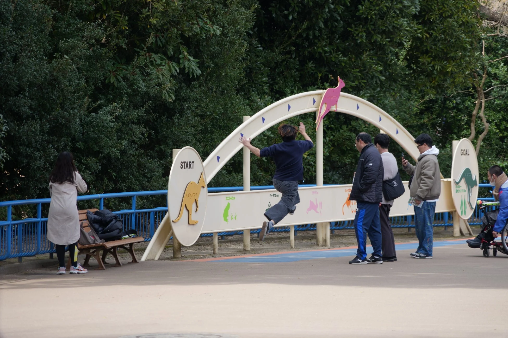 公園で動物のジャンプ距離を示す看板の下を飛び越える男性