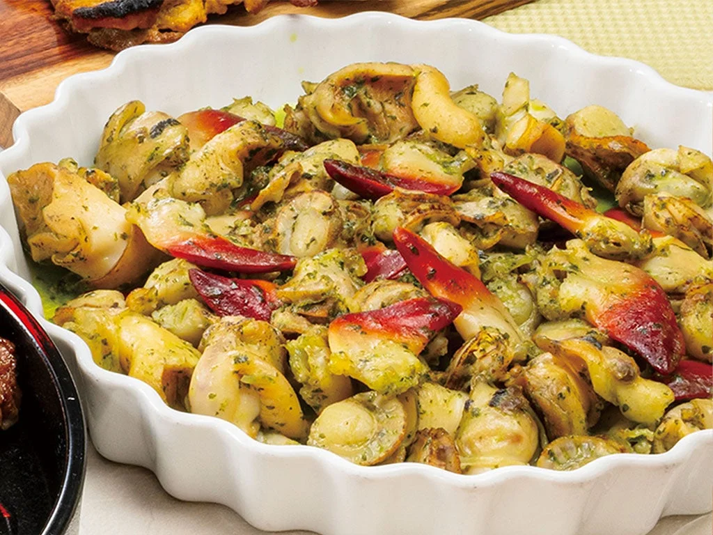 白い皿に盛られた、バジルソースで和えられた貝のシーフード料理