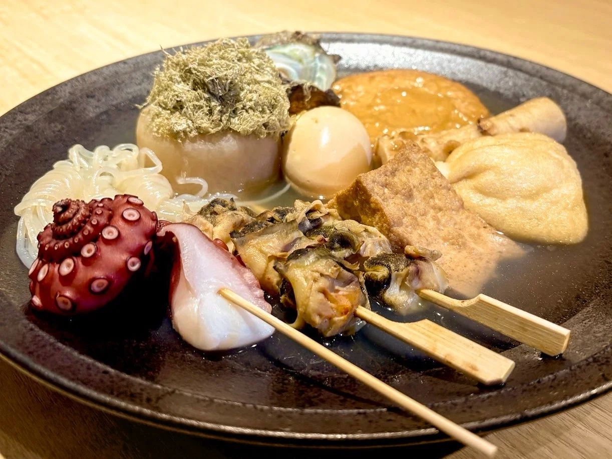 大根、たまご、タコ、つぶ貝など様々な具材が盛り付けられた、温かいおでんのクローズアップ写真です。